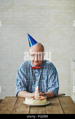 Mature man looking at birthday cake with burning candle on table Stock Photo