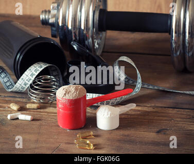 Whey protein powder in scoop with vitamins and plastic shaker on wooden background. Stock Photo