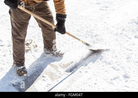 A man in winter ships and scrapes hard ice from the frozen driveway with a shovel Stock Photo