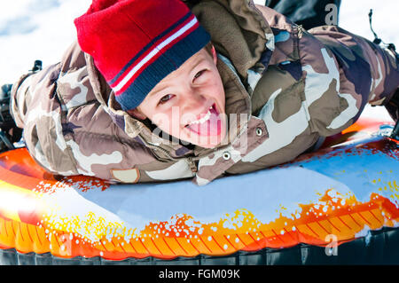 Cute boy riding snow tube up close sticking tongue out Stock Photo