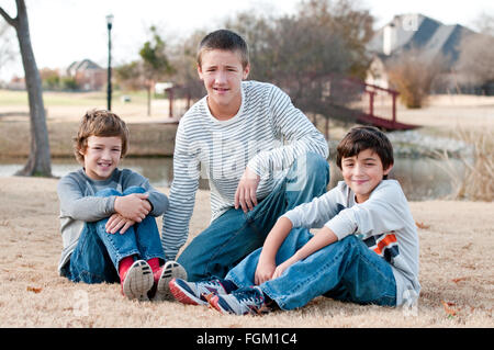 Group of three boys that are family and friends sitting on grass smiling. Stock Photo