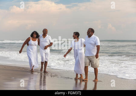 Happy romantic senior African American men and women couples laughing, walking, holding hands on a deserted tropical beach Stock Photo