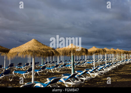 Sun loungers with umbrellas on a beach on stormy day Stock Photo