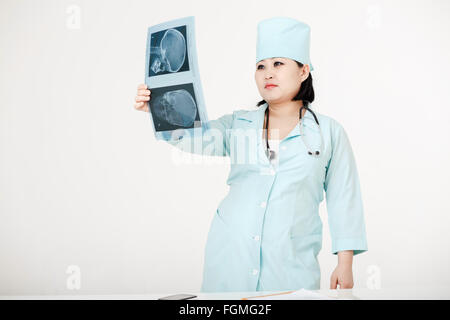 Young female Asian doctor with stethoscope looking at the x-ray. Nurse in a medical cap. Stock Photo