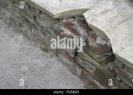 Broken concrete slabs on top of a crumbling, red sandstone wall Stock Photo