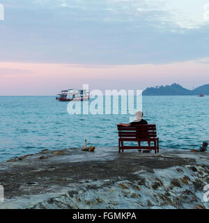 A lone young man sits on a bench at the seaside. Stock Photo