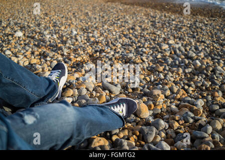 Legs of a woman wearing jeans sitting on Brighton beach,UK Stock Photo