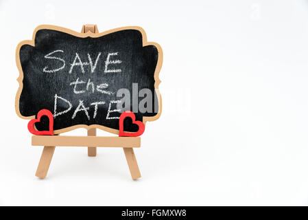 Wooden easel mini blackboard with faded chalk surface, text SAVE THE DATE and two red heart shape symbols, left hand side view, Stock Photo