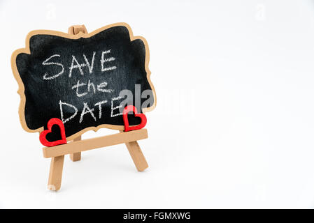 Wooden easel mini blackboard with faded chalk surface, text SAVE THE DATE and two red heart shape symbols, left hand side view, Stock Photo