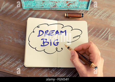Retro effect and toned image of a woman hand writing a note with a fountain pen on a notebook. Motivational concept with handwritten text DREAM BIG in speech bubble Stock Photo
