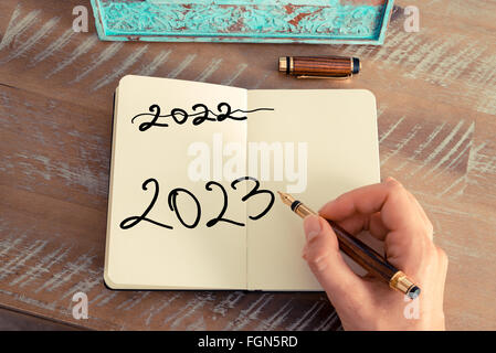 Retro effect and toned image of a woman hand writing a note with a fountain pen on a notebook. Motivational concept with Handwritten text Happy New Year 2023 and 2022 written off Stock Photo