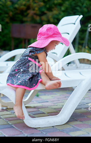 little girl in a red hat sits on a lounger Stock Photo