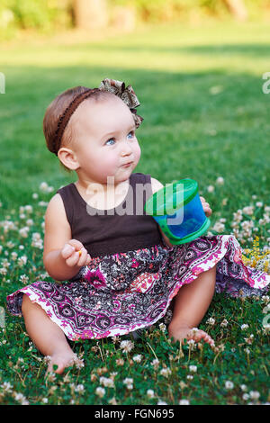 little girl sitting on the grass with a mug