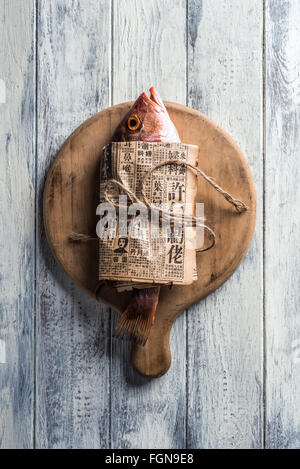 Red Snapper wrapped in Chinese newspaper on wooden background Stock Photo