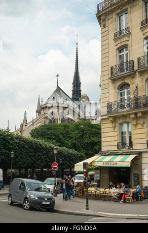 Patrons relax outdoors at the Esmeralda Cafe in Paris, with the Notre-Dame Cathedral in close view. Stock Photo