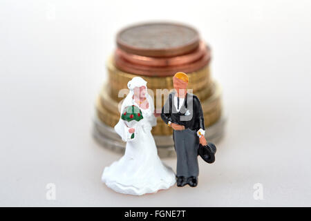 Bride and groom wedding couple figurines standing in front of coins stack Stock Photo