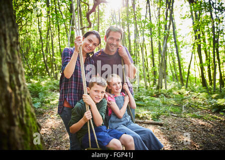 Portrait smiling family at rope swing in woods Stock Photo