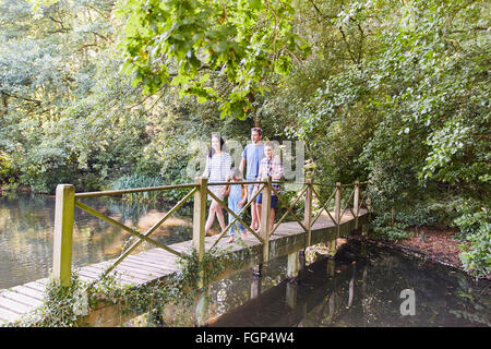 Family crossing footbridge in park with trees Stock Photo