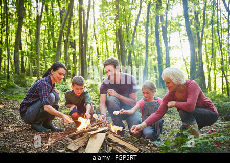 Multi-generation family roasting marshmallows at campfire in forest Stock Photo