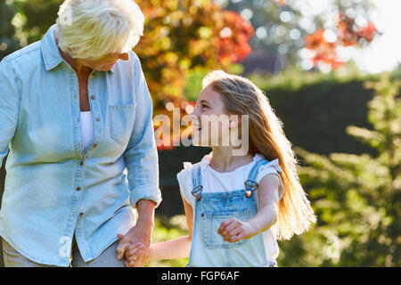 Grandmother and granddaughter holding hands and walking in sunny garden Stock Photo