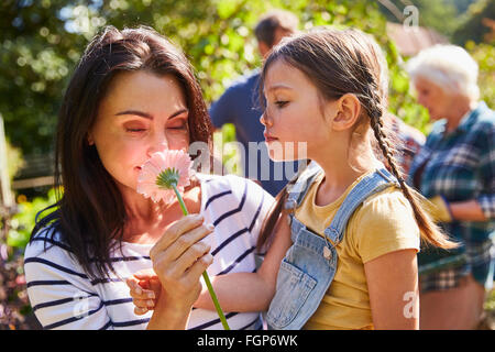 Mother and daughter smelling fresh pink flower in sunny garden Stock Photo