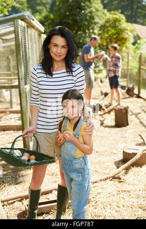 Portrait mother and daughter with basket of fresh eggs outside chicken coop Stock Photo