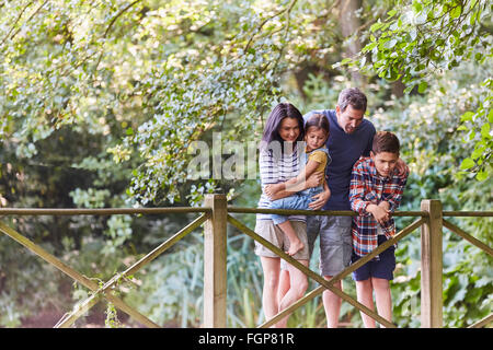 Family standing on footbridge in park with trees Stock Photo