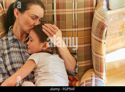 Tender mother cuddling sleeping daughter in armchair Stock Photo