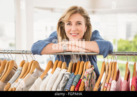 Smiling woman leaning on clothes rail Stock Photo