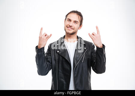 Smiling handsome young man in black leather jacket doing rock gesture over white background Stock Photo