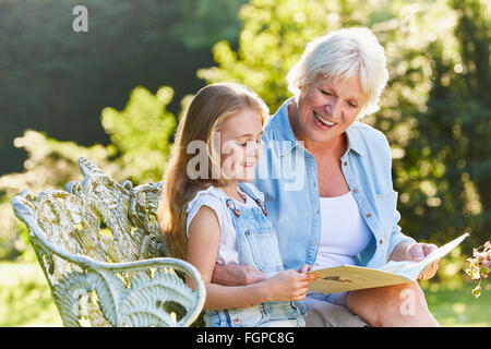 Grandmother reading with granddaughter on garden bench Stock Photo