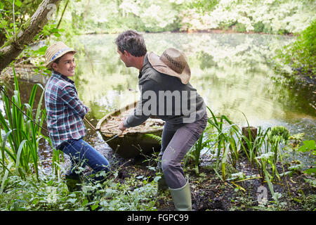 Father and son pulling boat to shore in pond Stock Photo