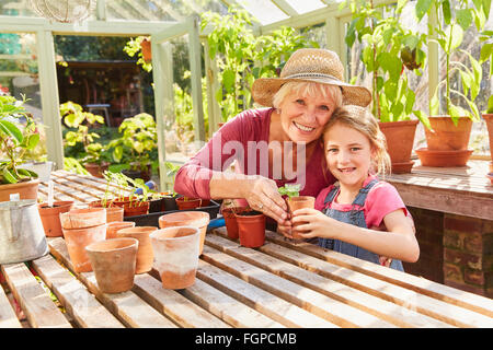 Portrait smiling grandmother and granddaughter potting plants in greenhouse Stock Photo