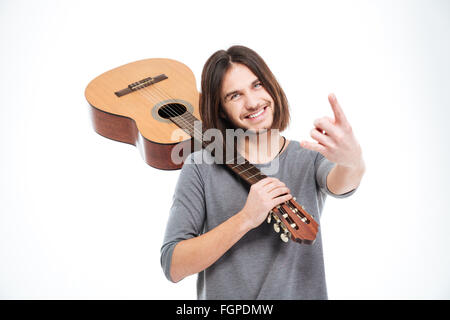 Cheerful young man holding guitar on his shoulder and doing rock gesture over white background Stock Photo