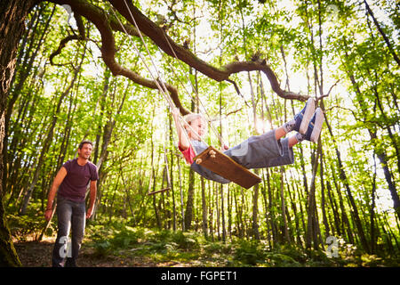 Father pushing daughter on rope swing in forest Stock Photo