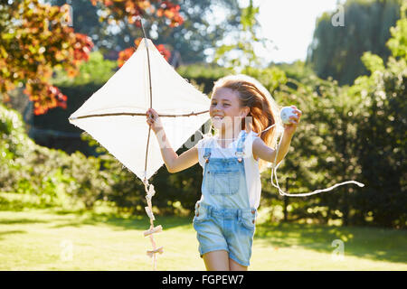 Enthusiastic girl running with kite in sunny garden Stock Photo