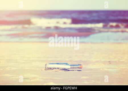 Vintage stylized message in a bottle on beach, shallow depth of field. Stock Photo