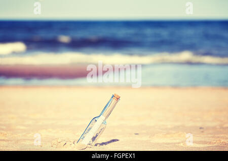 Vintage toned message in a bottle on beach, shallow depth of field. Stock Photo