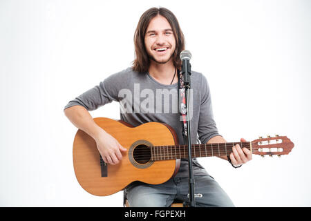 Smiling handsome young man with guitar singing in microphone over white background Stock Photo