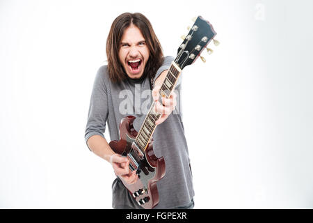 Excited popular young male singer with long hair shouting and playing electric guitar over white background Stock Photo