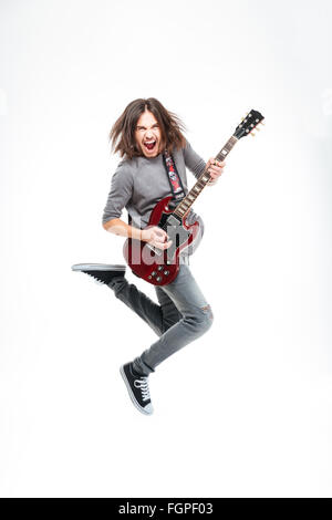 Happy young man with long hair jumping and playing electric guitar over white background Stock Photo