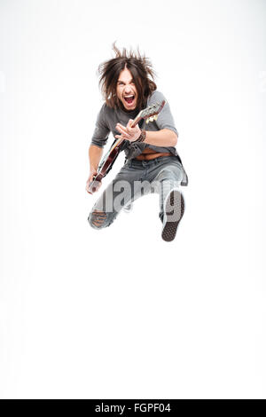 Excited joyful young male guitarist with electric guitar shouting and jumping over white background Stock Photo