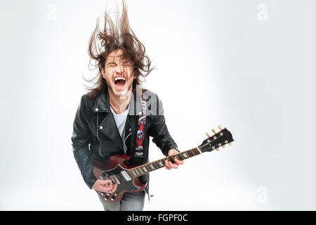 Excited young man in black leather jacket with electric guitar shouting and shaking head over white background Stock Photo