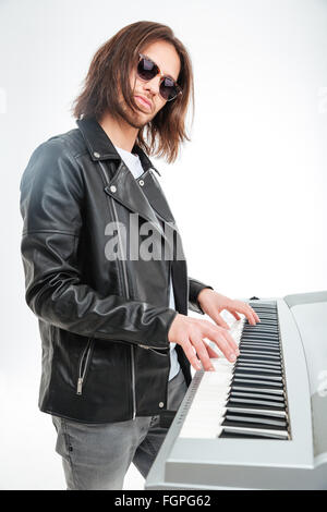 Confident young keyboardist in sunglasses standing and playing on synthesizer over white background Stock Photo
