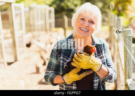 Portrait smiling woman holding chicken near coops Stock Photo