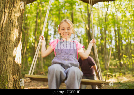 Portrait smiling girl swinging on rope swing in forest Stock Photo