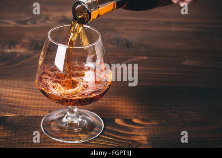 Pouring cognac or whiskey from the bottle into the glass against wooden background Stock Photo