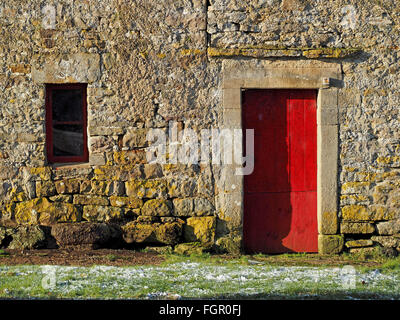 Old stone farm building with red door and window and frosty ground Stock Photo