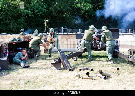 Vietnam war re-enactment. Rear view of two US 105mm howitzer artillery gun being re-loaded at fire base while under attack. Marines taking cover. Stock Photo