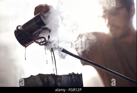 Blacksmith pouring steaming liquid over wrought iron Stock Photo